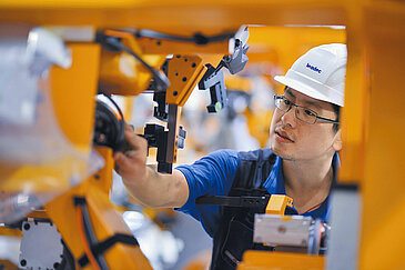 Leadec employee makes adjustments to robot arm.