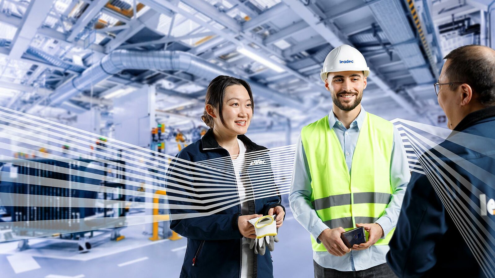 Three Leadec employees in workwear talking in front of a factory background. 