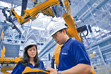 Two Leadec employees working at robot arms with controller. 