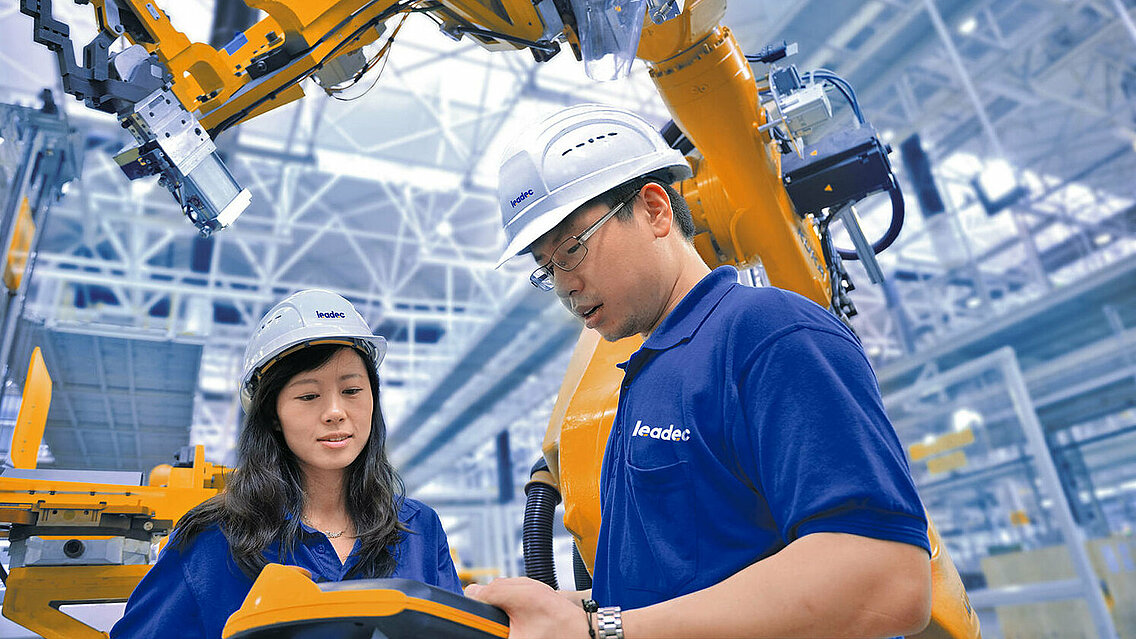 Two Leadec employees working at robot arms with controller. 