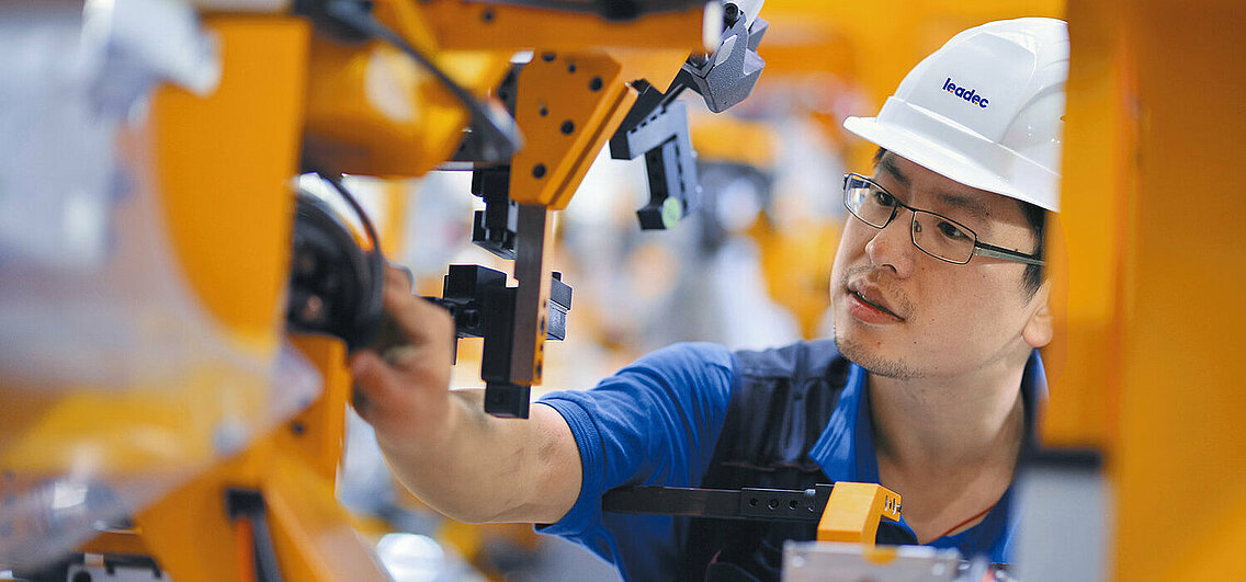 Leadec employee makes adjustments to robot arm.
